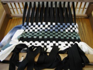 photo of a rigid heddle loom warped with black cotton twill tape and hand dyed fabric strips laid in as weft